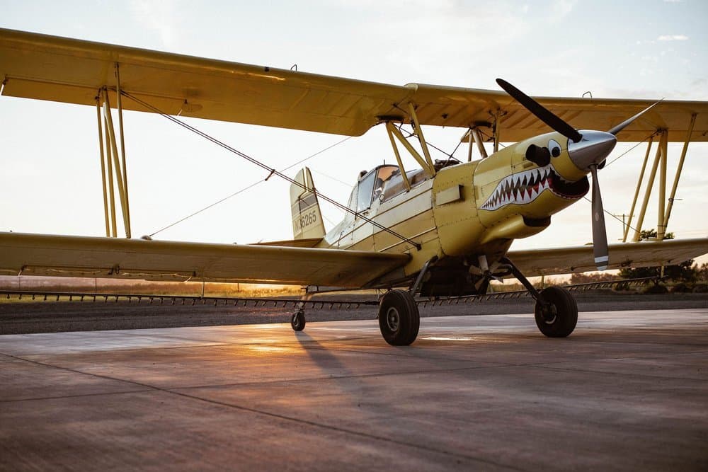 Yellow Ag Cat biplane with shark-mouth nose art parked on the ramp at sunset